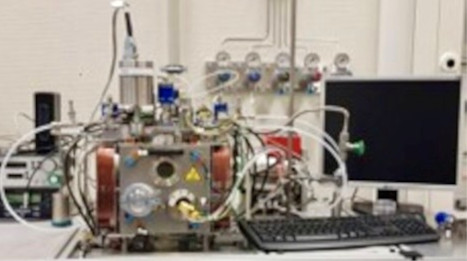 Laboratory device with multiple pipes, valves, and a monitor on a table.