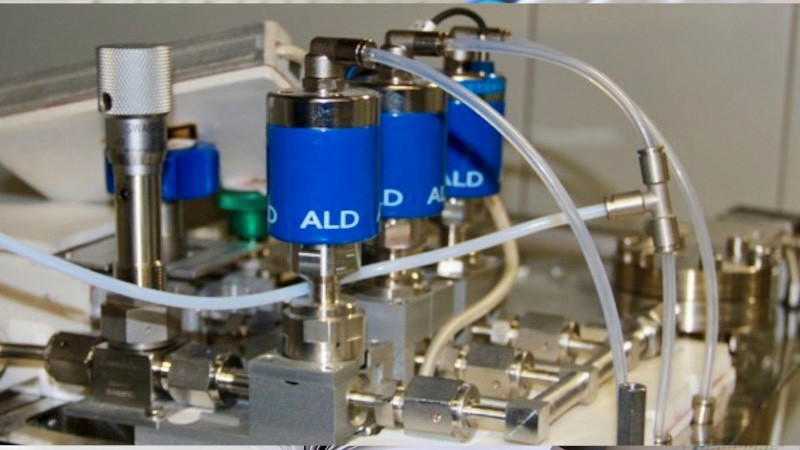 Close-up of a technical device with multiple blue cylinders connected by white tubes labeled 'ALD'