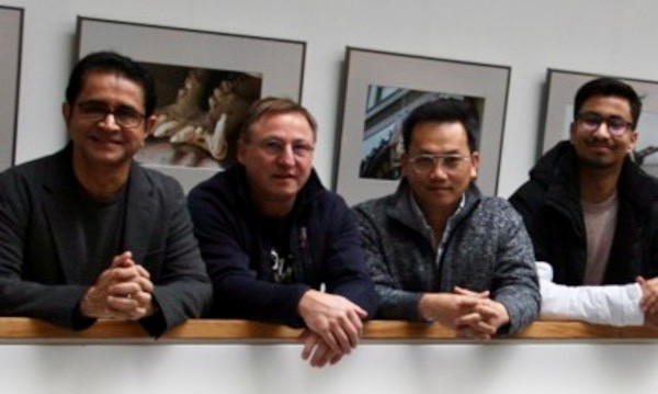 Four scientist of this research group leaning with crossed arms on a railing in front of a wall with framed pictures.