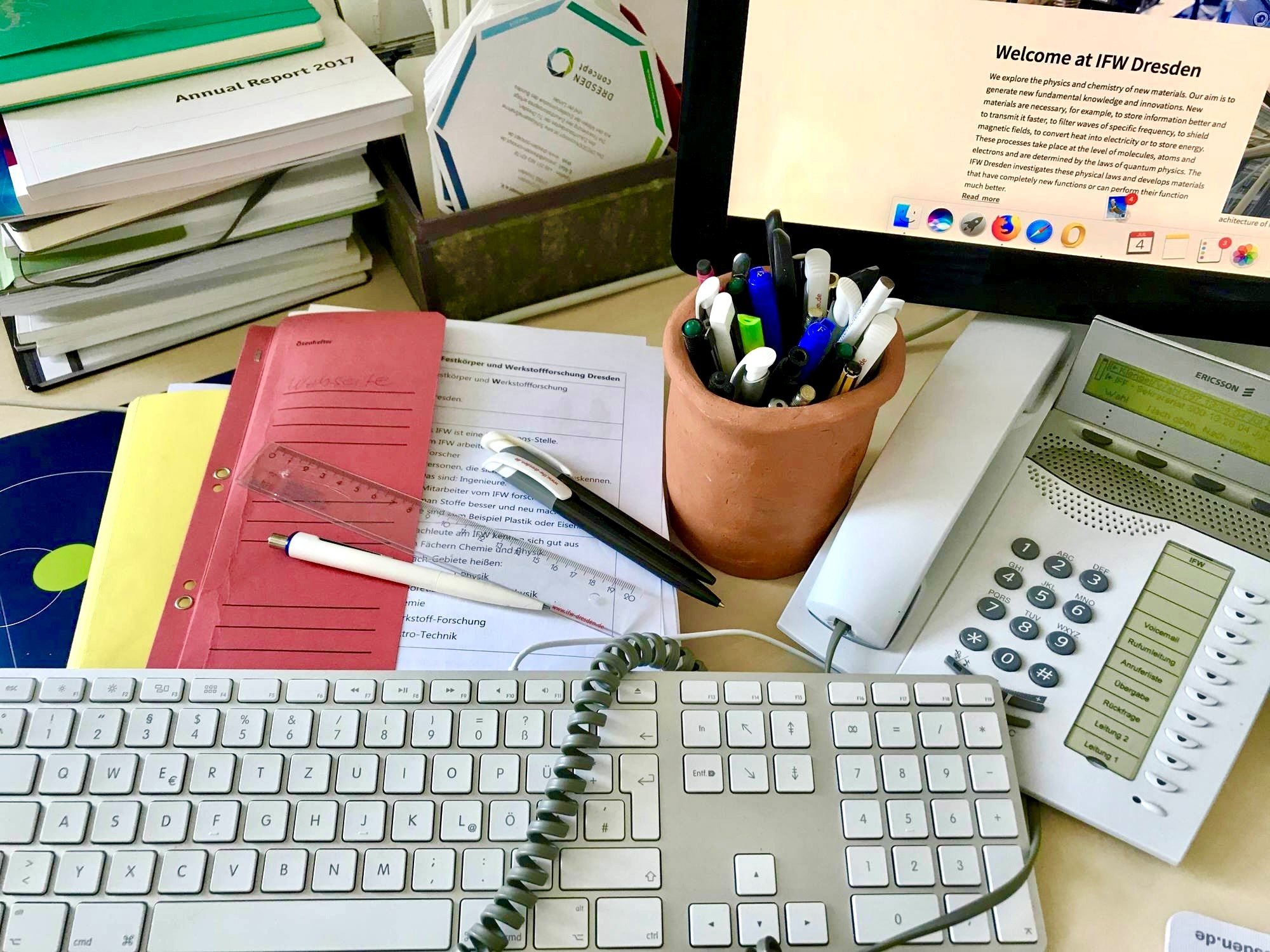 Office worker's desk with keyboard, telephone, pen holder, folders, and documents.