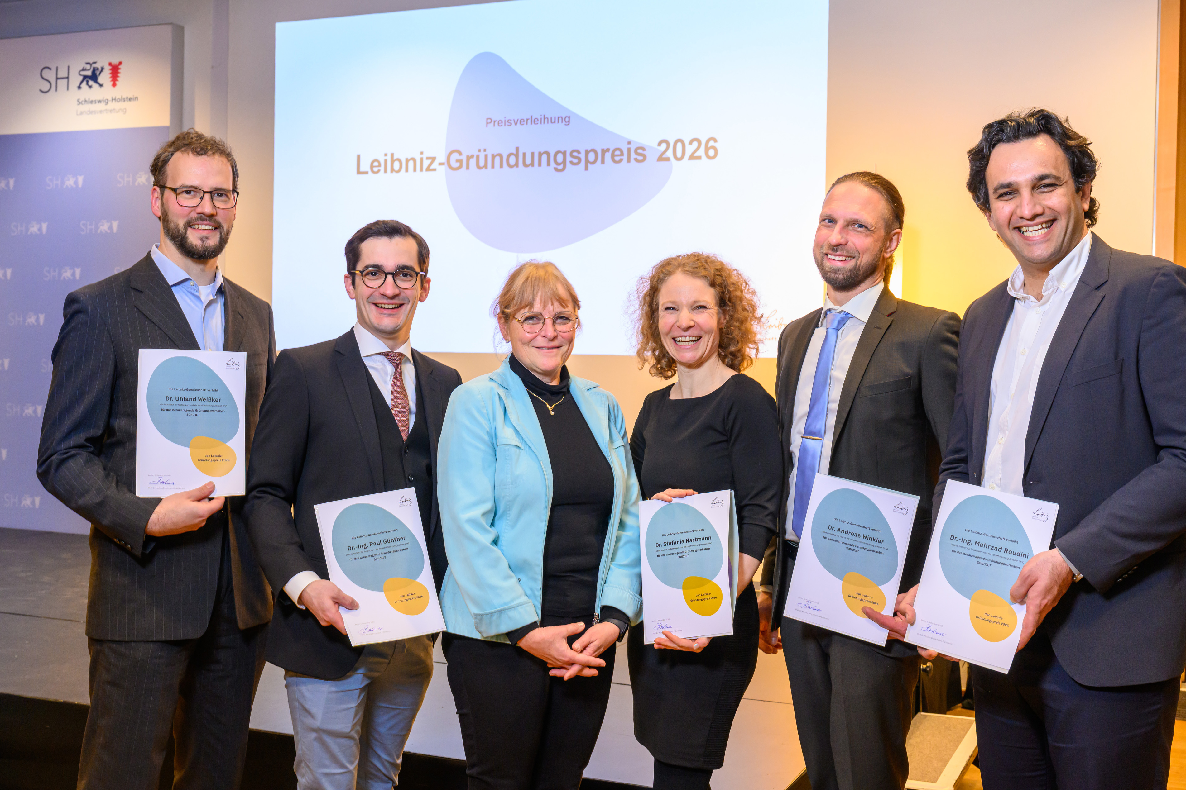Eine Menschengruppe mit einer Auszeichnung zum Leibniz-Gründungspreis 2026 in den Händen.